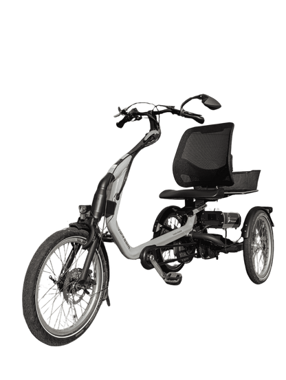 Een grijskleurige driewieler fiets met drie wielen. Een grote zit/ stoel om op te zitten en een grote mand achterop. Een spiegel op het stuur. Ook met elektrische ondersteuning en verlichting.